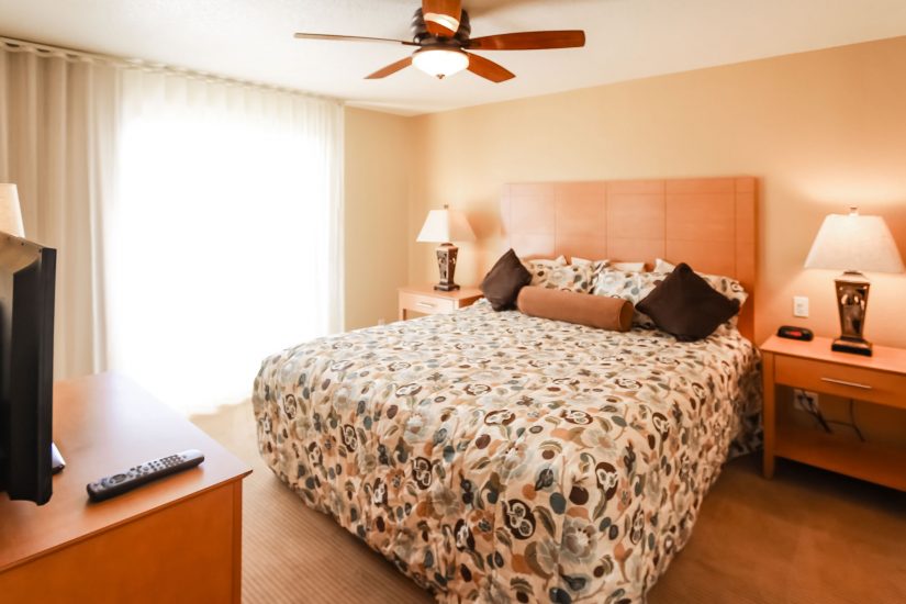 Photo of Bedroom Unit showcasing bed, side tables with lamps, ceiling fan, and side view of television.